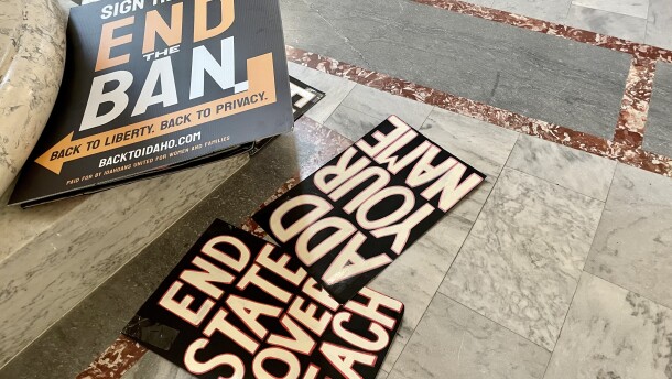 Signs strewn on the marble ground of the Capitol, one says "Sign here, end the ban. Back to liberty, back to privacy," "End State Overreach," and "Add your name." 