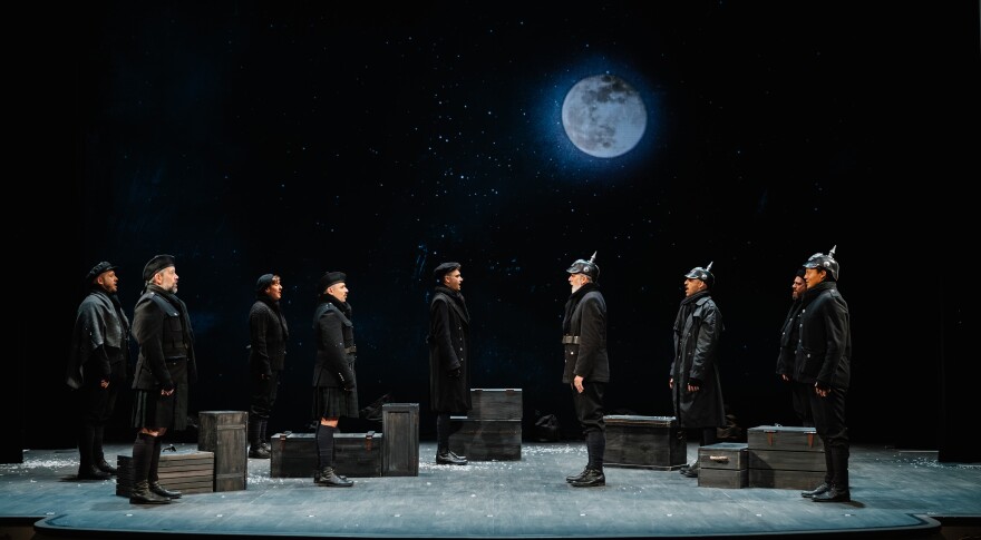 Men in World War I black uniforms face each other, standing on a stage.