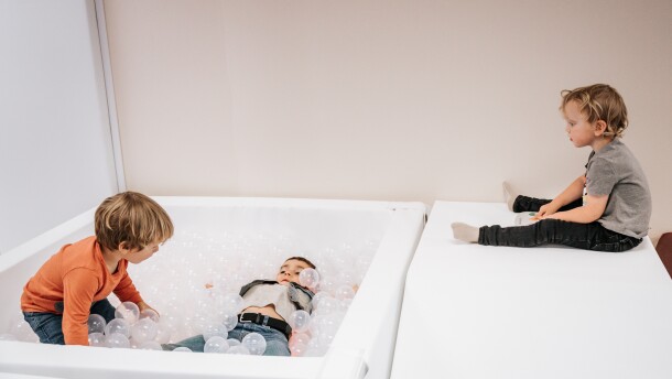 Three children are playing with a white ball pit, filled with clear plastic balls. 