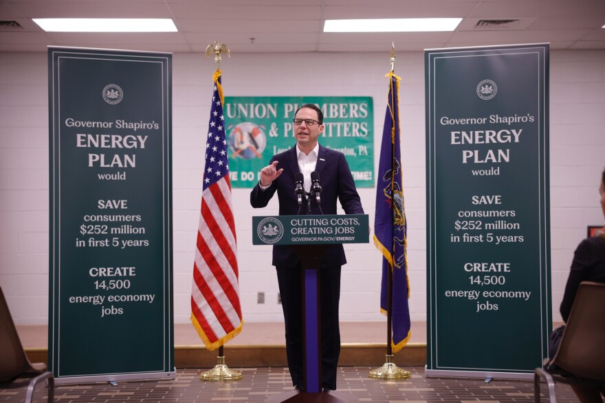 Josh Shapiro speaks at a lectern while flanked by sides promoting his energy plan.