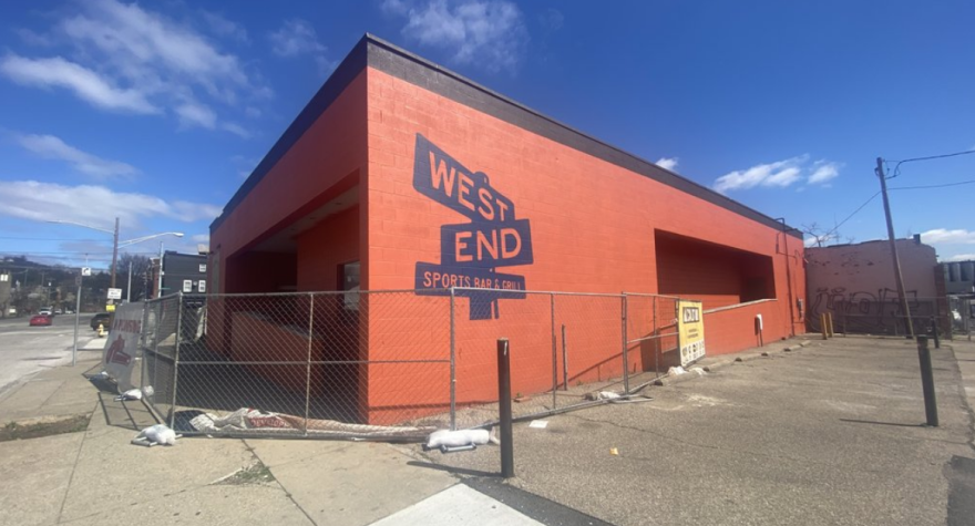 brown brick building behind fencing with "West End Sports Bar and Grill" painted on the side