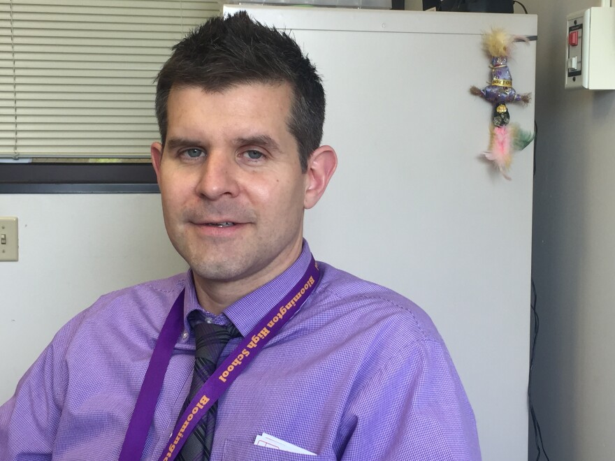 Man wearing a lanyard in a purple shirt in his office at Bloomington High School.