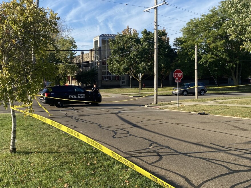 A black police car is parked at an intersection that's lined with police tape