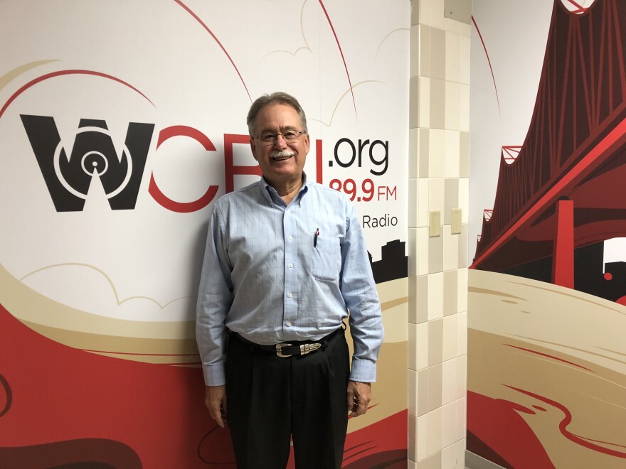 Peoria Area Association of Realtors president Bill McCarthy stands in front of the mural in the WCBU newsroom.