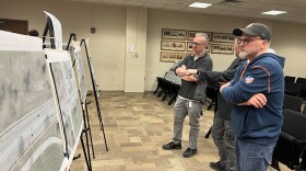 Three West Dayton community members gather around mock-ups of plans for reconstruction on W Third Street in Dayton's City Hall