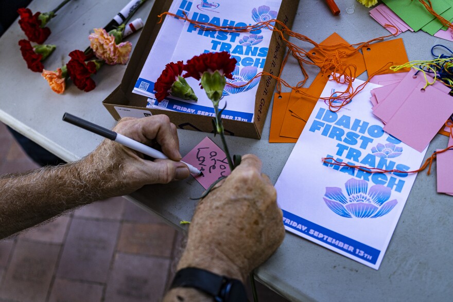 A pair of hands writing "you are loved" on a small pink piece of paper.