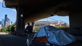 Seattle Stadium is seen in the background as a person rides a scooter past a series of tents on a trail near the stadium ahead of the 2026 FIFA World Cup soccer matches Wednesday, May 27, 2026, in downtown Seattle.