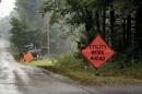 A stock photo shows an orange roadside sign warning of utility work ahead, with a heavy machine in the background carrying a large spool of cable.