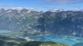A view from a high hill looking across a copper-colored body of water toward steep mountains on the other side.
