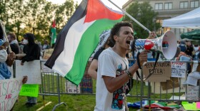 man shouts into loudspeaker while leading a group of protesters