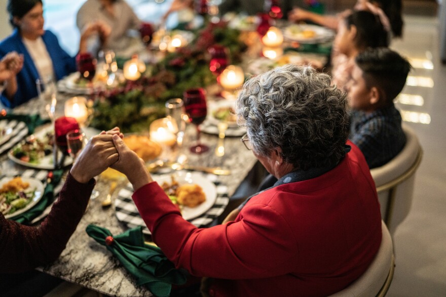 Elderly woman sits at a holiday dinner table holding hands with younger family members