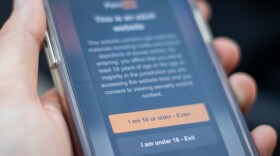 A hand holds a smartphone with age verification text on a pornographic website. 