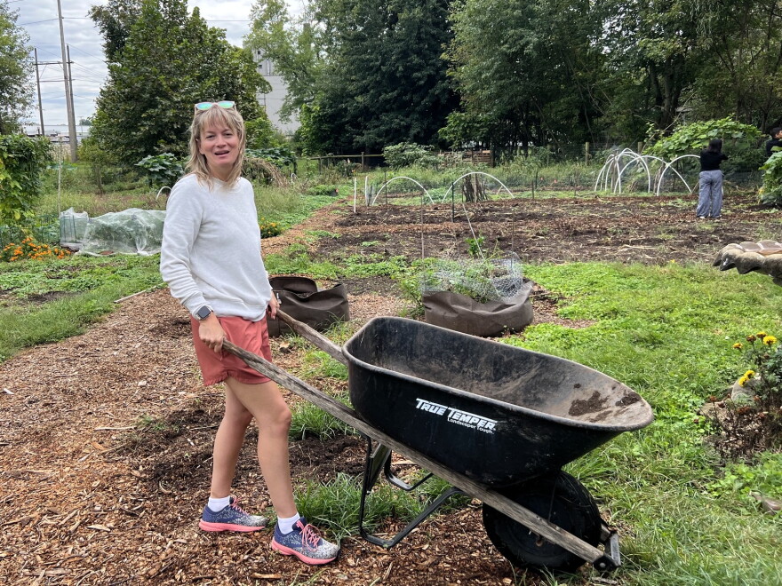 A woman stands with a wheelbarrow in a community garden.