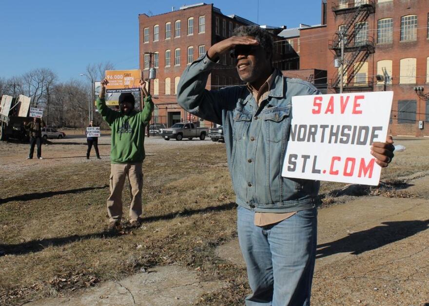 North St. Louis residents hold signs protesting the development. The sign in the foreground of the image reads, "SAVE NORTHSIDE STL . COM" 