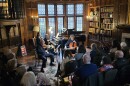 A piano trio performs in the library of the Rochester Academy of Medicine with a small crowd surrounding them