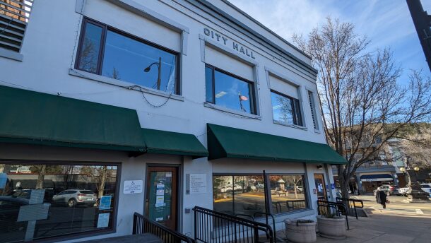 A two story grey building with large windows. A sign at the top of the building reads "city hall"