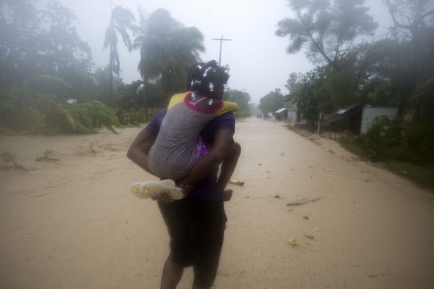 A woman carries a child through a waterlogged street as they head to a shelter under the pouring rain triggered by Hurricane Matthew in Leogane, Haiti, Tuesday, Oct. 4, 2016. Matthew slammed into Haiti's southwestern tip with howling, 145 mph winds tearing off roofs in the poor and largely rural area, uprooting trees and leaving rivers bloated and choked with debris. (AP Photo/Dieu Nalio Chery)