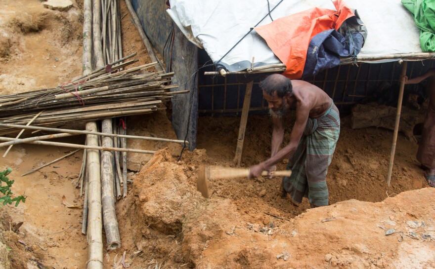 Rohingya refugee Shah Miya digs at the sand that inundated his shelter. Despite the threat of more landslides, he says he doesn't want to move.