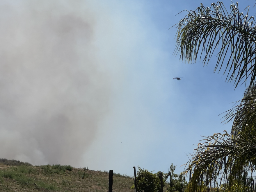 A helicopter flies through heavy smoke from the Sandy Fire on May 18, 2026.