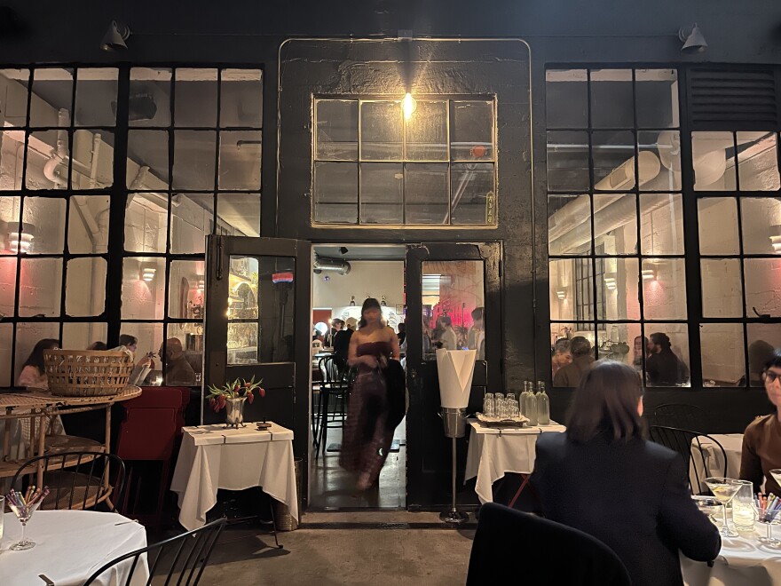 A waiter walks through the door of Friends and Family onto the patio at night.