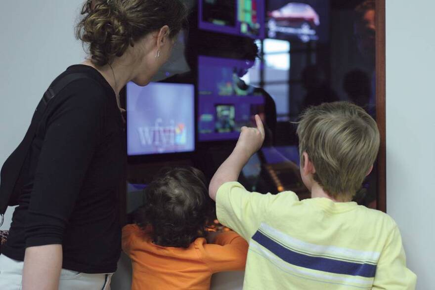 TV production open house with adult woman and 2 children looking at a master control room with tv monitors and contrl boards