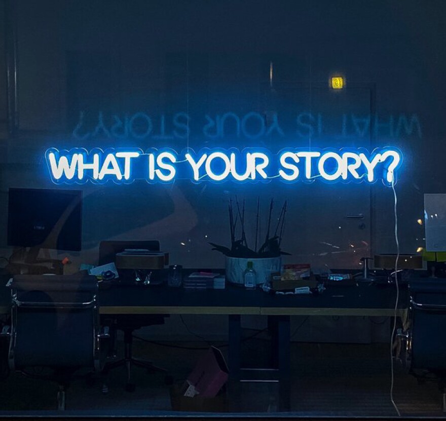 “What Is Your Story” neon sign in window.