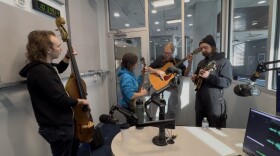 Four musicians play inside a small recording studio.