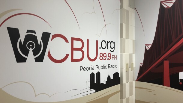 A mural in the entry hallway at the WCBU newsroom in Morgan Hall on the Bradley University campus shows the station's branding logo and depictions of the Peoria skyline and the Murray Baker Bridge. 