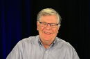 A man with a grey shirt and glasses smiles at the camera.