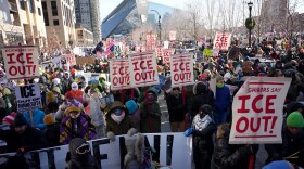People protest against federal immigration agents holding signs outdoors along a city street
