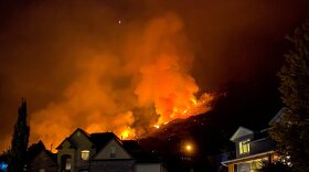 Photo of flames and smoke burning on a hill behind houses.