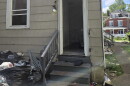 A rear entrance to a single family home. The door and a window are wide open and trash is piled on the ground.