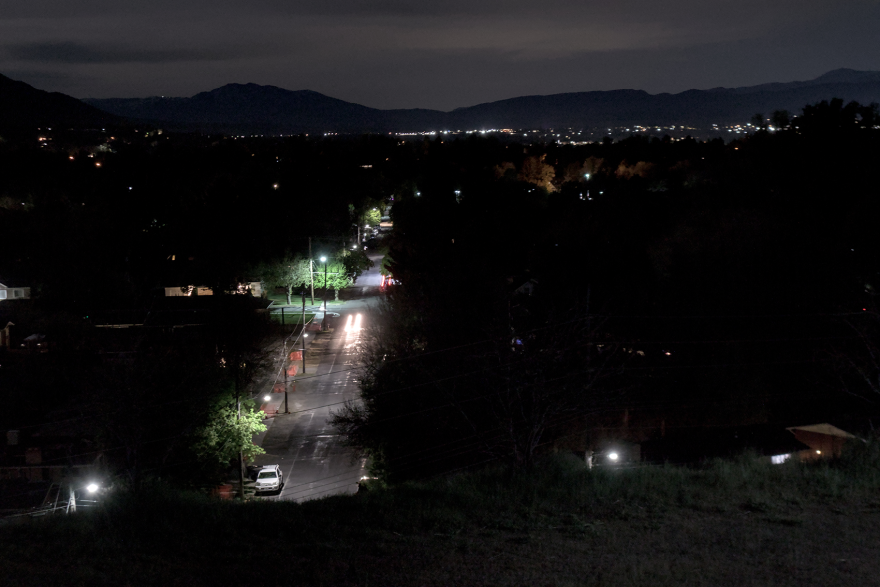 Streetlights illuminate a street under the darkness of night. The light goes down toward the street, not up toward the sky.