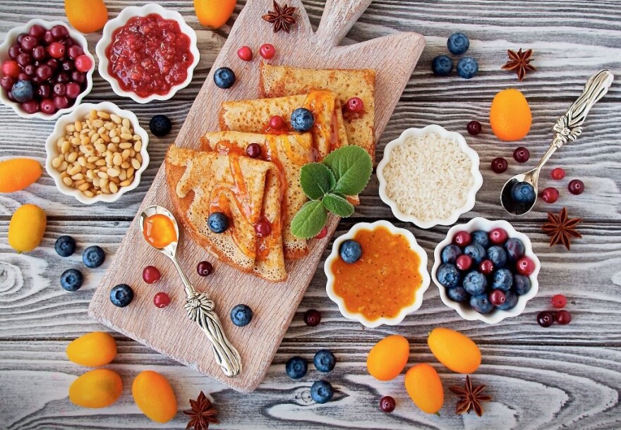 Wooden board with gluten-free crepes surrounded by jams and fruits