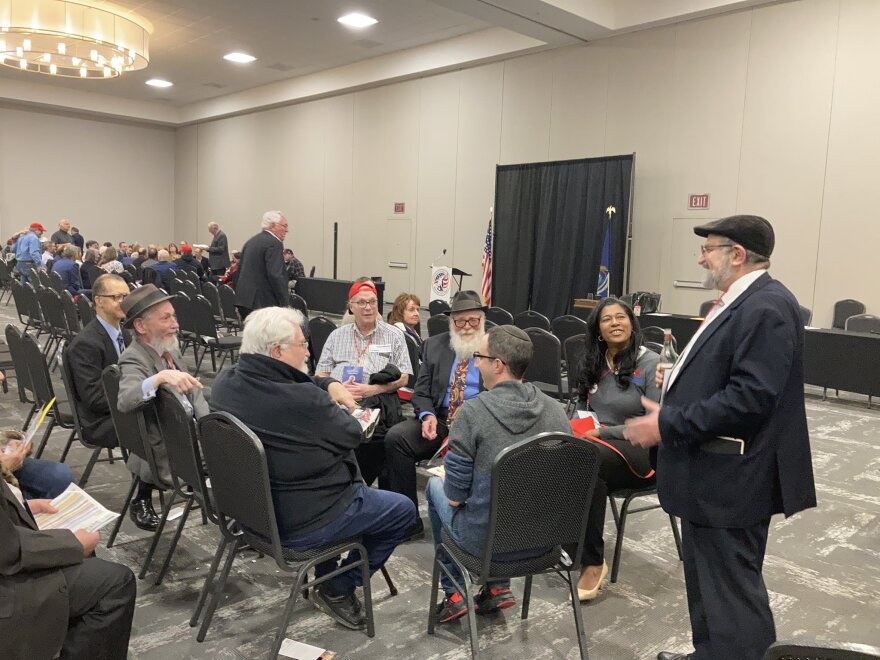 A group of people sit in a circle of black chairs in a conference center talking. One of them is secretary of state candidate Kristina Karamo. 