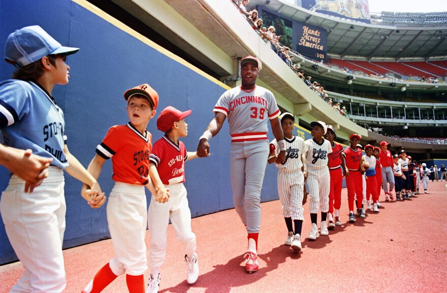 a man in a baseball uniform holds hands with a line of children also in baseball uniforms