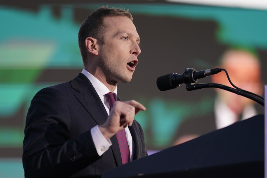 a man in a suit stands speaking at a microphone