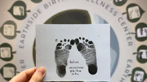 A hand is shown holding up a piece of paper showing baby ink footprints.