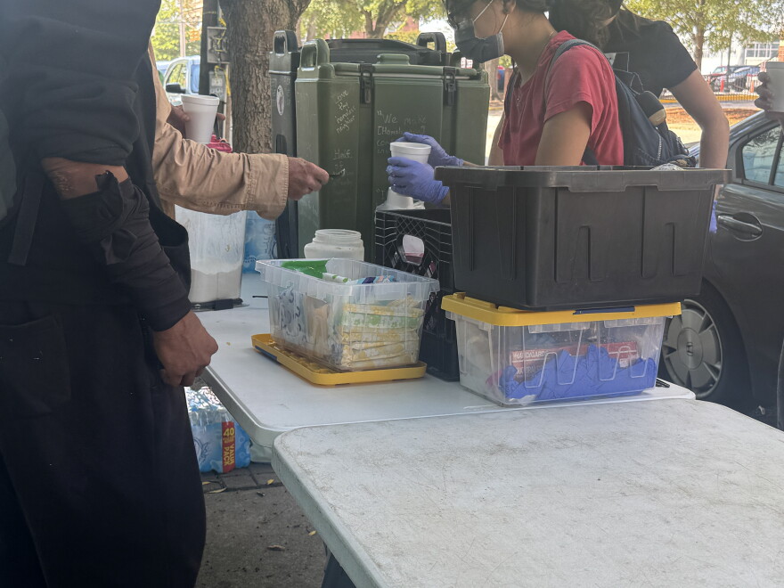 A portion of Food Not Bombs Midlands’ table, including feminine hygiene products, water and coffee, set up outside Richland Library Main in downtown Columbia.