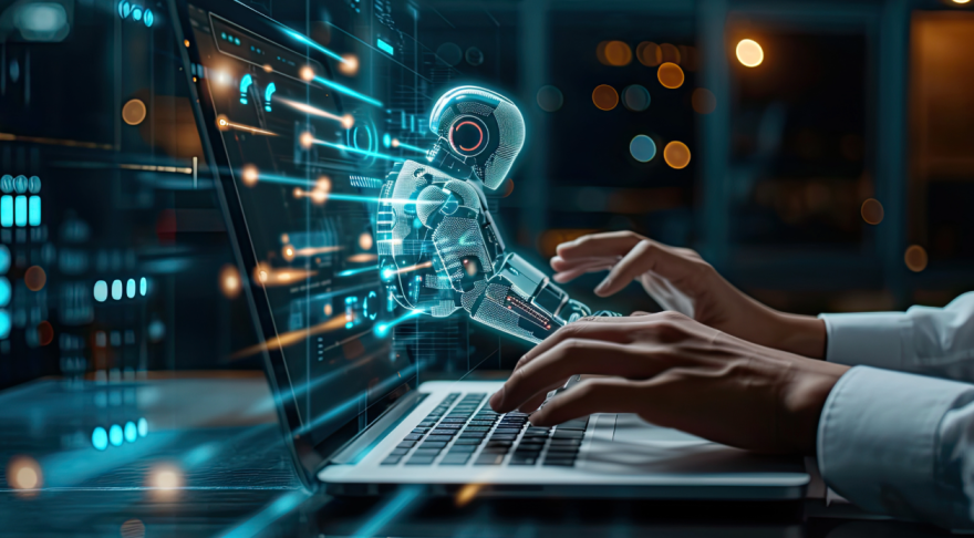 An image of a human with hands above a laptop computer keyboard and a ghostly image of a robot emerging from the screen of the laptop