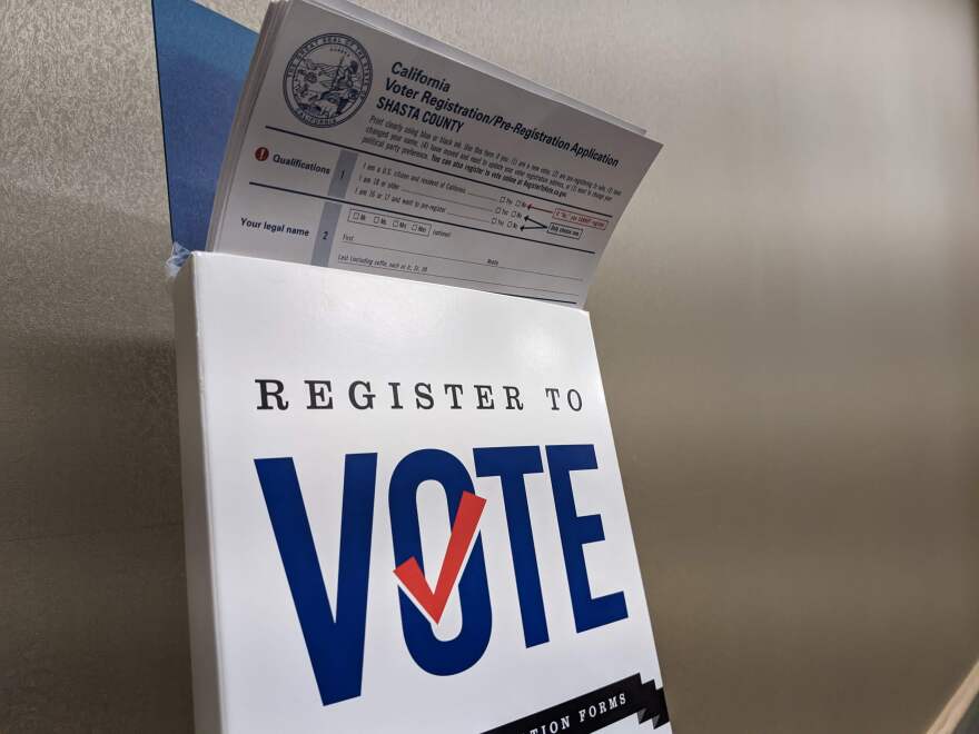 A number of Shasta county voter registration applications held in an upright stand. The stand reads "Register to vote"