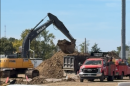 a yellow backhoe dumps dirt into a truck parked next to red pickup trucks