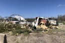 Three semi trucks are covered with tree and siding from the destroyed recycling center. 