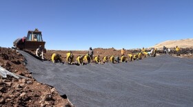 Line of people unroll grey material over dirt