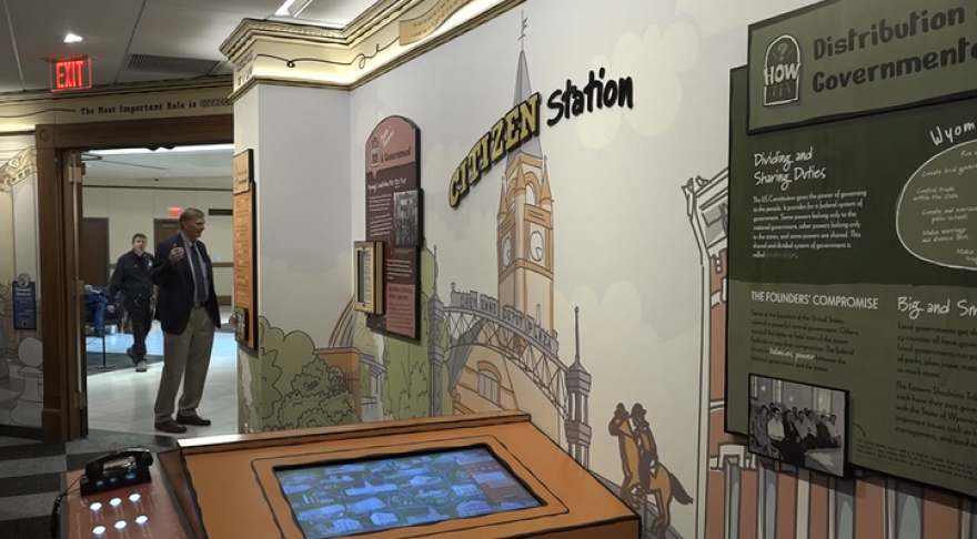 A painted wall says, "Citizen station," with panels about the three branches of government. In the foreground is an interactive display and corded telephone.