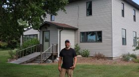 A man in his forties wearing a black shirt stands in front of his home, which has stood for over a hundred years.