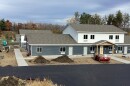 A group of housing united under construction with a newly paved roadway in front and autumn trees in the background.