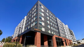 A 8-story grey and brick apartment building on a corner.