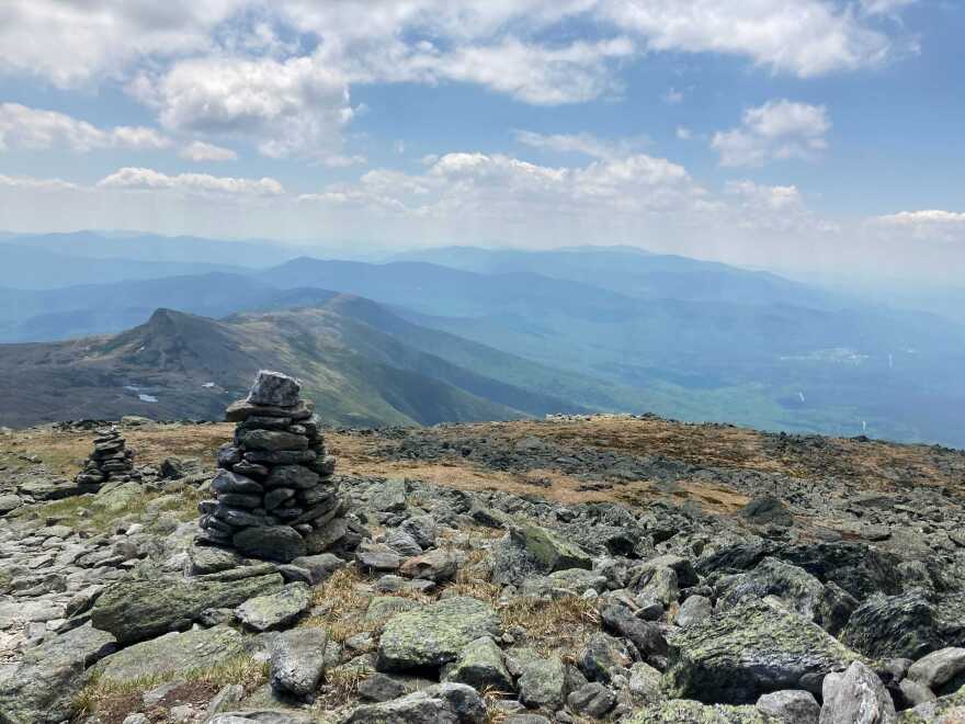 A cairn in front of an alpine slope with the White Mountains of New Hampshire in the background