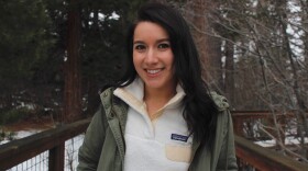 Karina Gonzalez is standing in front of a forest and looking at the camera and smiling.
